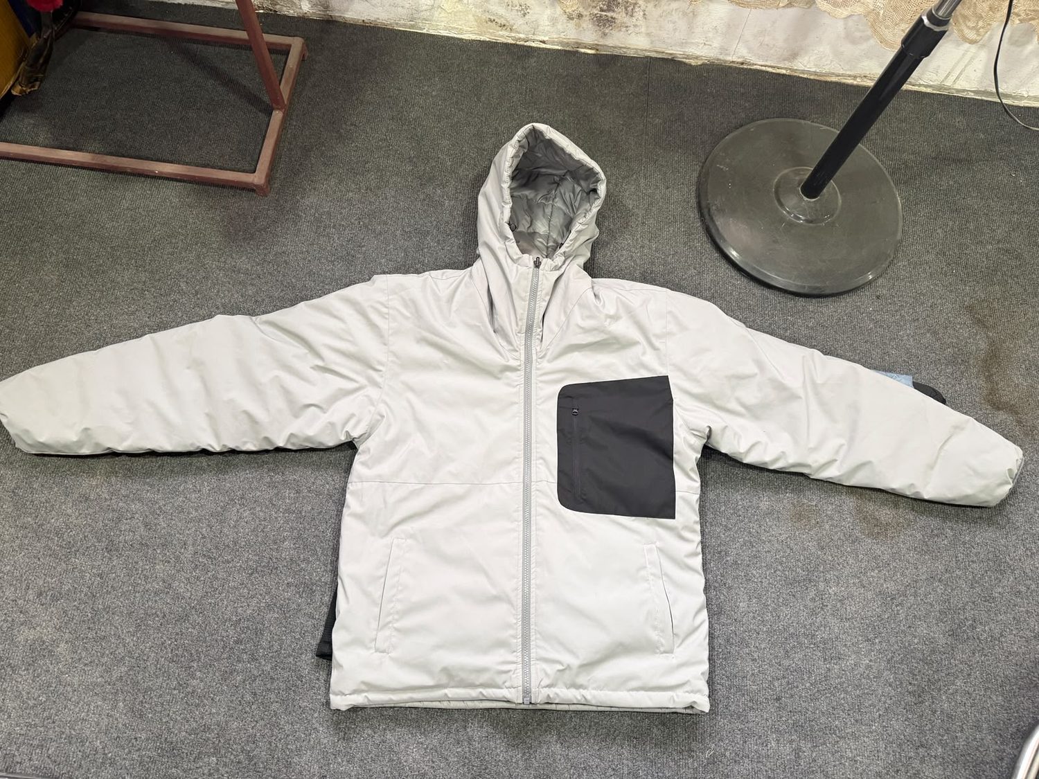 An off white hooded jacket laid flat with a large black chest pocket panel