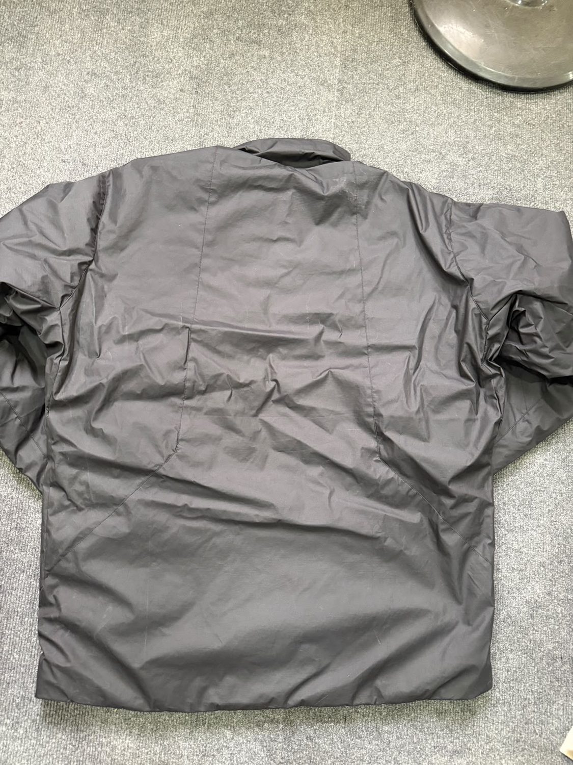The back of a grey shell jacket laid flat on a workroom floor