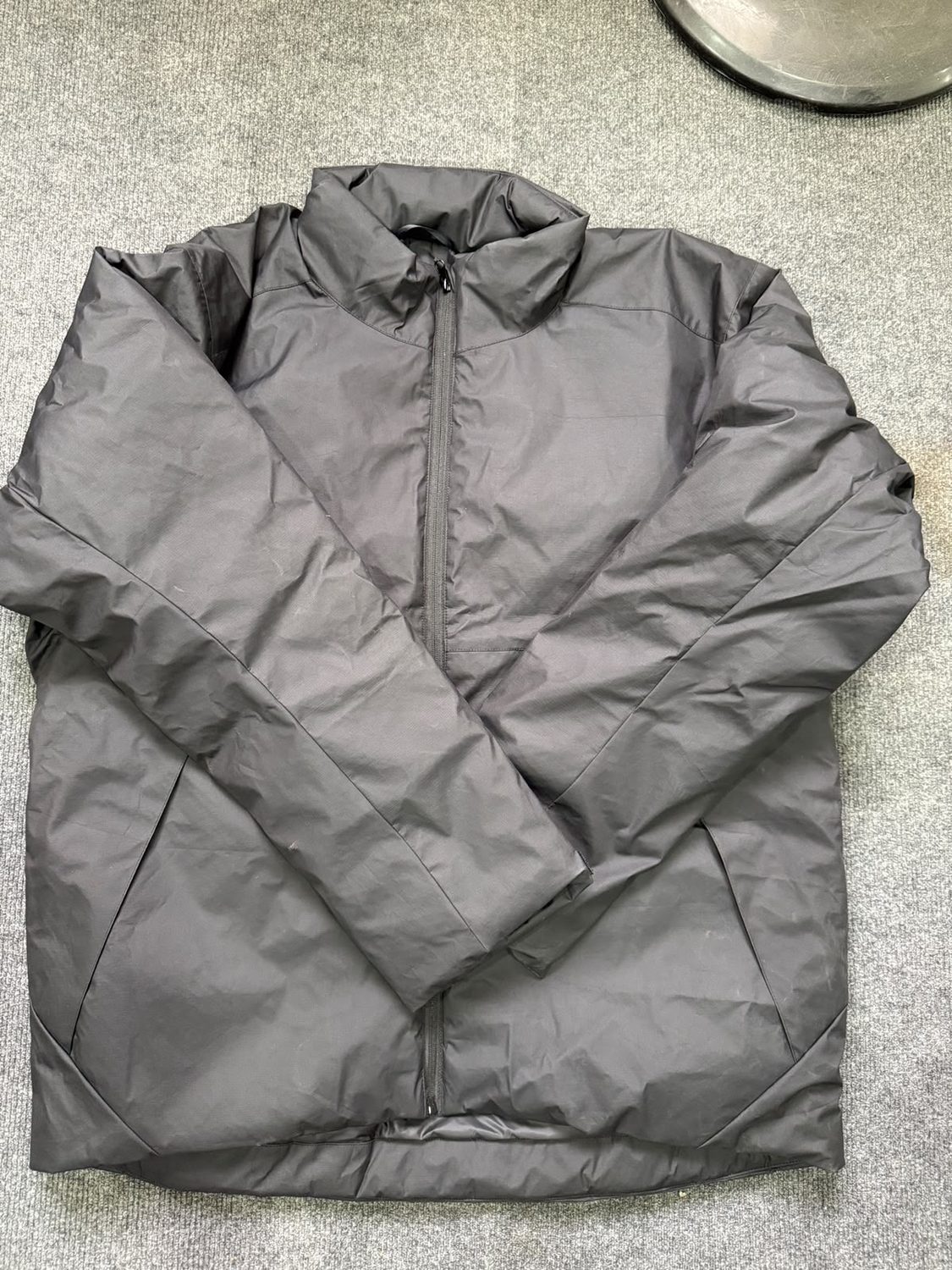 A grey hooded shell jacket laid flat, front zip closed